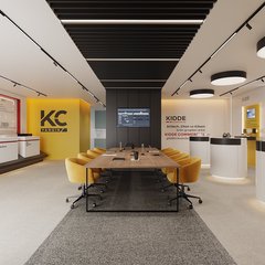 Showroom: uzun ahşap toplantı masası ve sarı sandalyeler, solda sarı KC duvarı ve yangın alarm sergi paneli, siyah lamelli tavan, sağda beyaz silindirik sergi bankoları ve ekranlı sarı nişler