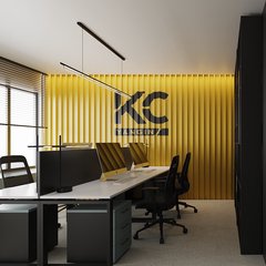 Açık ofis: sarı lamel duvarda KC logosu, dört kişilik beyaz tablalı siyah ayaklı çalışma masaları, solda jaluzili pencere; sağda kapalı ofisin noktalı cam bölmesi
